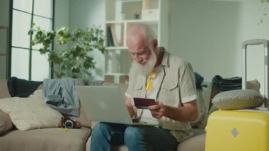 Mutlu yaşlı bir adam pasaportundan bilgisayara veri giriyor. Gülümseyen Yaşlı Adam Yolculuğa Hazırlanıyor, İnternette Başarı İçin Seviniyor. Online rezervasyon. Kış Maceraları.
