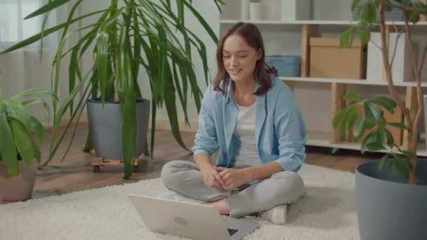 微笑的年轻女子坐在花坛地板上的笔记本电脑前 植物改善心情和幸福 女人在家工作 在家学习 女人上网聊天 女人打视频电话 — 图库视频影像