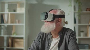 VR gözlüklü, gri sakallı, modern bir yaşlı adam çevredeki her şeyi inceler. VR gözlüklü yaşlı bir adam yaşlılara yardım etmek için Home.VR 'daki masada oturuyor..