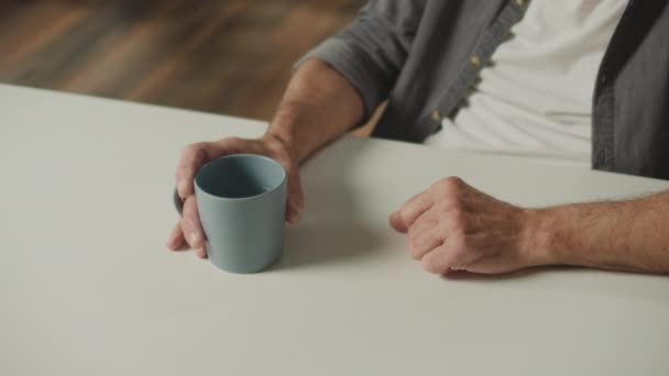 お茶を飲みながら男性の手のクローズアップ 古い男の手は天然ミネラルウォーターでマグカップを保持します 高齢者のためのお茶 飲料水の利点 — ストック動画