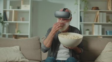 VR gözlüklü, gri sakallı, modern bir yaşlı adam çevredeki her şeyi inceler. VR gözlüklü yaşlı bir adam patlamış mısır yiyor. Yaşlılara Yardım İçin VR.