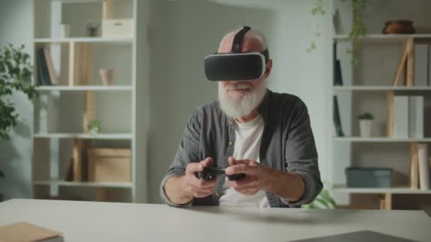 Vr眼镜中的老人 中的一个老人拿着一根棒子玩电脑游戏 坐在桌旁 一个现代老人玩Playstation 增强型现实与老年人游戏 — 图库视频影像
