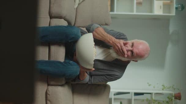 一个老年人吃爆米花 专心致志看电视 一个严肃的老人坐在沙发上看一部非常有趣的电影 电影及其角色 — 图库视频影像