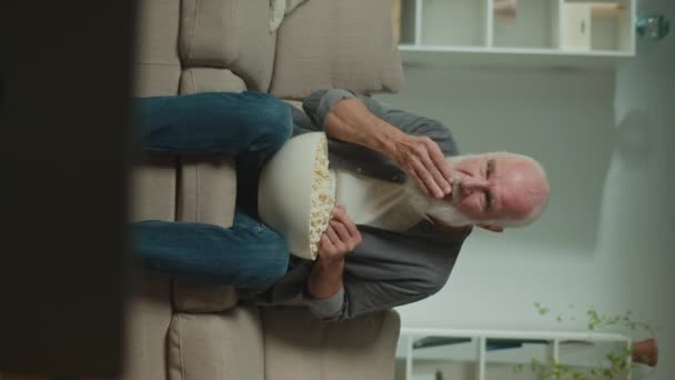 一个老年人吃爆米花 看体育节目 一个严肃的老年人坐在沙发上庆祝体育胜利 电影作为一种放松和心理救济的形式 — 图库视频影像