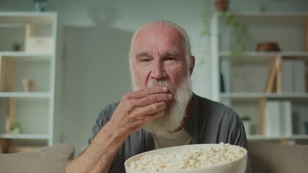 Anciano Comiendo Palomitas Concentrándose Ver Televisión Anciano Serio Sentado Sofá — Vídeos de Stock