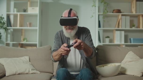 Vr眼镜 中的一位老人用棒子玩电脑游戏 坐在沙发上吃爆米花 增强型现实与老年人游戏 — 图库视频影像