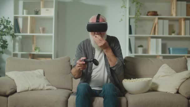 Anciano Gafas Juega Juegos Ordenador Con Joystick Sentado Sofá Comiendo — Vídeo de stock