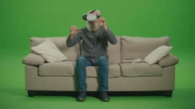 Yeşil Ekran. VR gözlüklü yaşlı bir adam her şeye dokunur ve inceler, koltukta oturur. Yaşlıların Sosyalleşmesi için sanal gerçeklik. Özürlü Yaşlılara Yardım İçin VR.