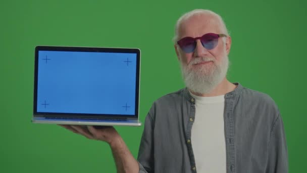 绿色屏风 一个戴着滑稽眼镜的老人用蓝色屏风指着他的笔记本电脑的画像 网上购物的老年人 安老院及安老院的互联网 — 图库视频影像
