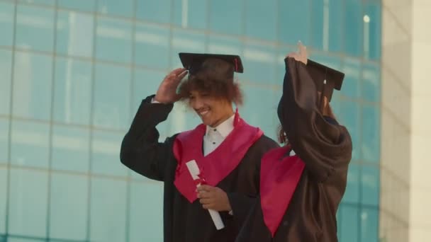 ポジティブ成功した卒業生は 大学の背景を歩いている間に卒業キャップを投げます 一緒に素晴らしいと感じています 卒業式の瞬間のコンセプト — ストック動画