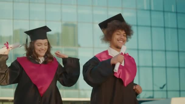 ディプロマ カレッジとダンスをする2人のポジティブな成功した卒業生 感情的な卒業式の日 卒業式の瞬間のコンセプト — ストック動画