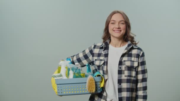 一个穿着黄色橡胶护目镜 面带微笑的年轻女子的画像 她拿着一个装有清洁用品的盒子 在灰色背景上显示出一个不错的标志 方便宠物的清洁方法 — 图库视频影像