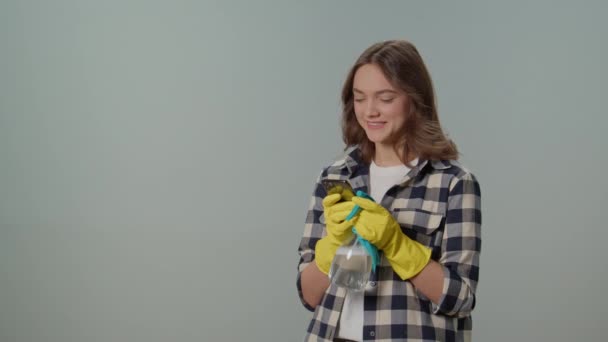 一位戴着黄色手套 头戴喷雾器和智能手机的快乐的年轻女性 在灰色背景下对手机的成功感到欣喜 — 图库视频影像