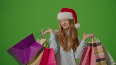 Yeşil Ekran. Noel Baba Şapkalı Kız Heyecanla Noel Hediyelerini Gösteriyor. Bayram çılgınlığı, mevsimlik alışveriş ve Noel kutlamalarının atmosferi. Tatil Alışveriş Sprei