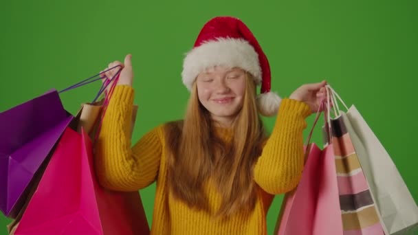 绿色屏风 穿着圣诞老人帽子的女孩兴奋地展示了她的圣诞购物 节日的法国人 季节性的购物 圣诞庆典的气氛 假日购物摊位 — 图库视频影像