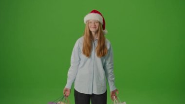Yeşil Ekran. Noel Baba Şapkalı Kız Heyecanla Noel Hediyelerini Gösteriyor. Bayram çılgınlığı, mevsimlik alışveriş ve Noel kutlamalarının atmosferi. Tatil Alışveriş Sprei