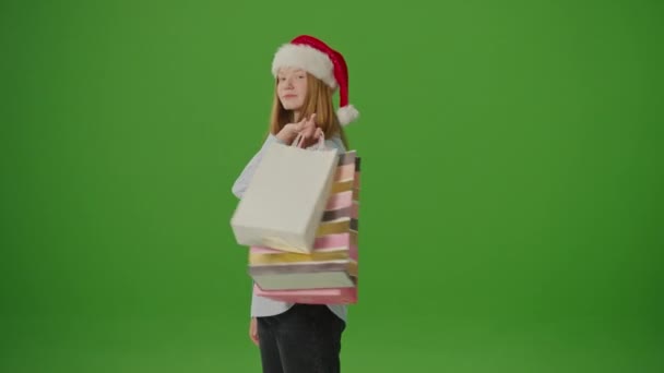 绿色屏风 穿着圣诞老人帽子的女孩兴奋地展示了她的圣诞购物 节日的法国人 季节性的购物 圣诞庆典的气氛 假日购物摊位 — 图库视频影像