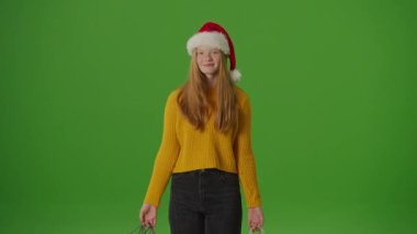 Yeşil Ekran. Noel Baba Şapkalı Kız, Noel alışveriş çantalarını neşeyle gösteriyor. Bayram ruhuna şenlikli bir bakış mevsimlik alışverişlerin ve kutlamaların heyecanını yakalıyor.