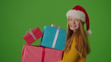 Yeşil ekran. Çekici Noel Baba Şapkalı Genç Kız gülümseyerek ayakta duruyor ve elinde bir sürü hediye kutusu tutuyordu. Kutlamanın Ruhu 'nu somutlaştıran Neşe saçıyor