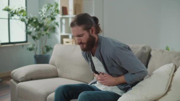 ソファーに座っている男性は 突然胃に痛みを感じました 胃をマッサージすることで痛みを和らげようとする男 — ストック動画