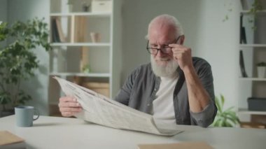 Gülümseyen, zeki yaşlı bir adam masaya oturur ve gazete okur. Elinde gazete gülüşü olan yaşlı bir adam gazetede haberleri ve güncel olayları görür, gazete konseptinde.