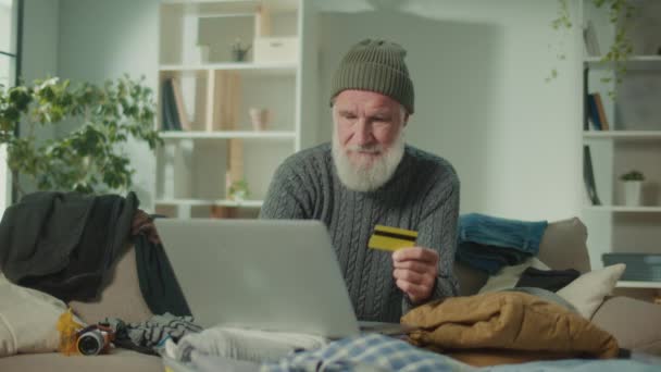 快乐的老人旅行者在网上商店用信用卡购物 一个年长的男人在帽子里买东西 网上交易 — 图库视频影像