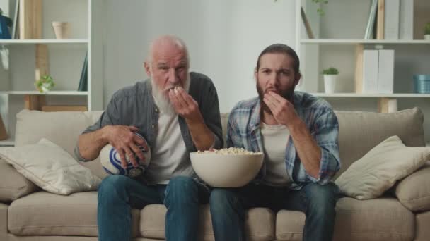 Starszy Młody Towarzysz Kanapie Piwo Popcorn Ręku Głęboko Zaangażowany Swoje — Wideo stockowe