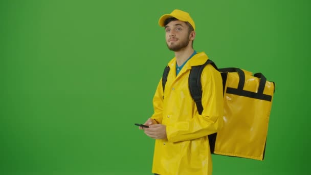 身穿黄色制服 背着热背包 用智能手机检查订货的绿色屏风青年送餐者 向客户发送订单途中的快递员 后视镜 — 图库视频影像