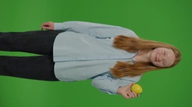 Yeşil Ekranı Böl. Dikey Videolu Genç Kız, elma yerken gülümsüyor, somutlaşıyor. Sağlıklı Yeme ve Okul Beslenme. Günlük Diyetlerinde Besleyici Seçimleri Kucaklayan Gençliğin Canlı Bir Göstergesi