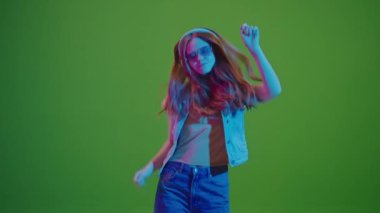 Yeşil Ekran. Neon ışıklarla dans eden genç kız, kulaklıklarından müzik dinliyor. Modern, dijital bir ortamda gençlik enerjisi ve müzik tutkusunun canlı bir gösterimi