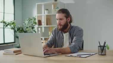 Bilek ağrısı. Bir adam laptopta çalışırken aniden bileğinde ağrı hissetti. Yaralı koluna diğer eliyle dokunuyor. Ofis sendromu konsepti. Klavye Kullanmaktan El Ağrısı.