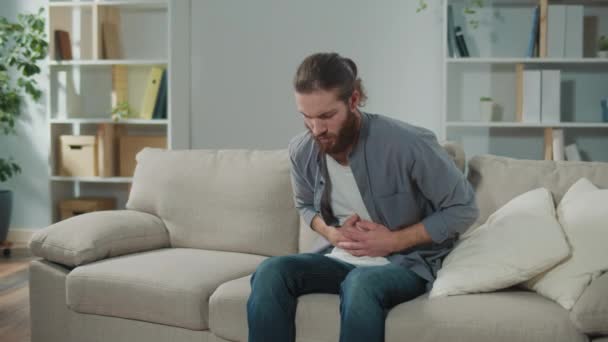 ソファーに座っている男性は 突然胃に痛みを感じました 胃をマッサージすることで痛みを和らげようとする男 — ストック動画