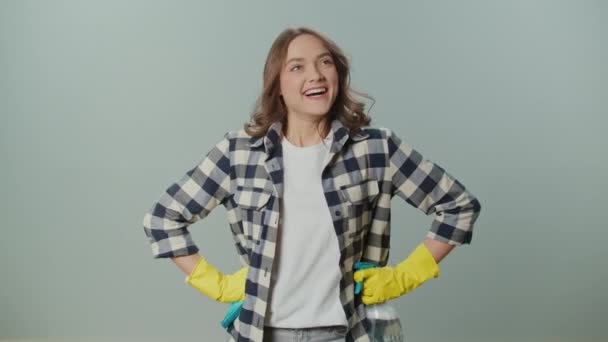 一个穿着黄色手套 拿着一个清洁喷雾器和抹布的年轻女子的画像 对她在灰色背景上的清洁结果感到满意 — 图库视频影像
