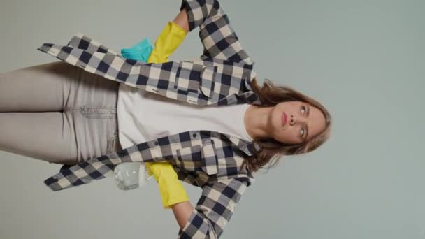 一个穿着黄色橡胶护目镜的疲惫的年轻女人 拿着一个喷雾器 在灰蒙蒙的背景上放着破布 多功能清洁工具 数字工具的智能清洁 — 图库视频影像