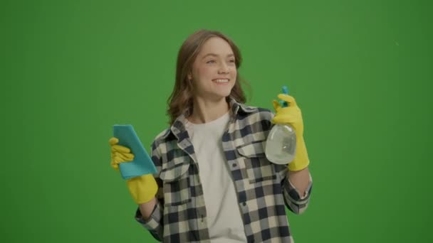 绿色屏风 一个戴着黄色橡胶护目镜 面带微笑的年轻女子的画像 手里拿着一个清洁喷雾器和破布 一位女家庭主妇正在准备打扫房间 最低限度清洁 — 图库视频影像