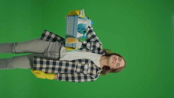 垂直视图 绿色屏幕 一个身穿黄色橡胶护目镜的微笑的年轻女子拿着一个装有清洁用品的盒子 对自己的清洁效果感到满意 — 图库视频影像