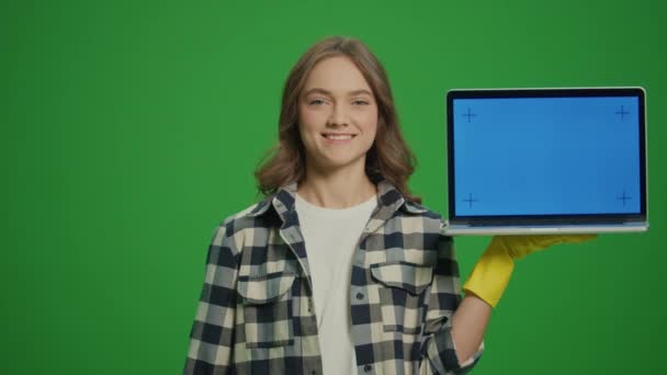 緑色のスクリーン 黄色い保護手袋とクリーニング製品の笑顔の若い女性の肖像画は ブルースクリーン付きのラップトップを保持しています 仮想クリーニングと生産性のコンサルティング — ストック動画