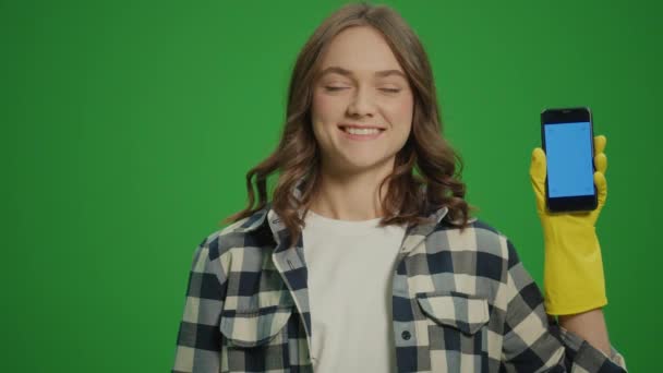 绿色屏风 一个身穿黄色橡胶护目镜 头戴清洁产品 面带微笑的年轻女子的画像 一个女家庭主妇拿着一个蓝屏智能手机 智能清洁技术 — 图库视频影像