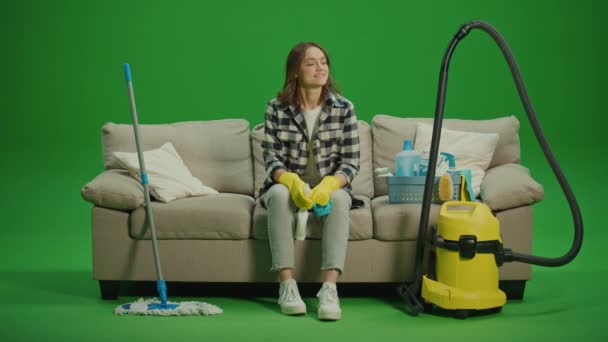 绿色屏风 一位穿着黄色橡胶护目镜 面带微笑的年轻女子坐在沙发上 对自己的清洁结果感到满意 整理及存放清洁用具 — 图库视频影像