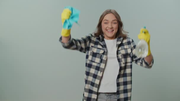 一个穿着黄色手套的快乐的年轻女人的画像 拿着一个清洁喷雾器和抹布 为灰色背景的清洁的成功感到高兴 智能清洁技术 — 图库视频影像