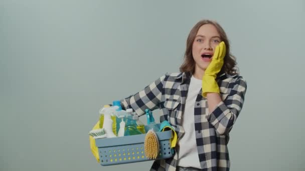 一位穿着黄色手套的惊讶的年轻女性的画像 她在灰色的背景上拿着一个装有清洁用品的盒子 一位女家庭主妇正准备清扫 民政事务处的组织架构建议 — 图库视频影像