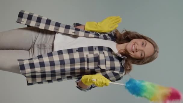 一个穿着黄色手套 面带微笑的年轻女子的画像 在灰蒙蒙的背景上带着一个垃圾桶跳舞 一位女家庭主妇正准备清扫 多项任务清洁日常工作 — 图库视频影像