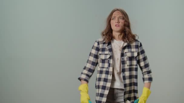 穿着黄色手套 手握清洁喷雾器和抹布 双手放在灰色背景上的年轻女性家庭主妇肮脏而烦躁 清洁应用效率及恒久性 — 图库视频影像