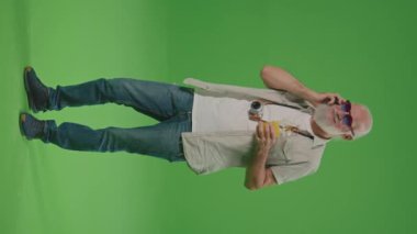 Dikey Görünüm. Yeşil Ekran. Kokteylli Komik Gözlüklü Mutlu Yaşlı Bir Adam Telefonda Konuşuyor ve Geleceğe Bakıyor. Emeklilikte Seyahat.