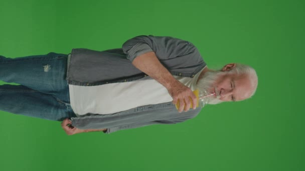 縦のビュー グリーン スクリーン 笑顔の老人はジュースでオレンジカクテルを飲む 高齢者は喉が渇いていると感じ 冷たいジュースを飲む 健康的なライフスタイル — ストック動画