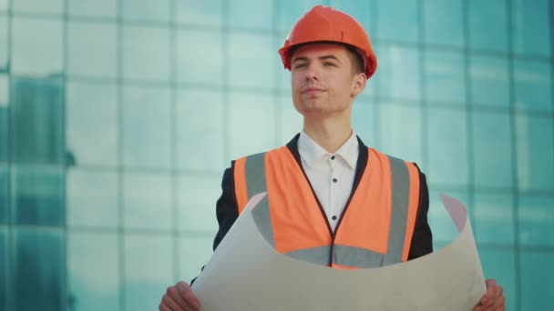 身穿护目镜和安全夹克的男性工程师或建筑师 手拿着施工图纸走在蓝窗大楼附近 — 图库视频影像