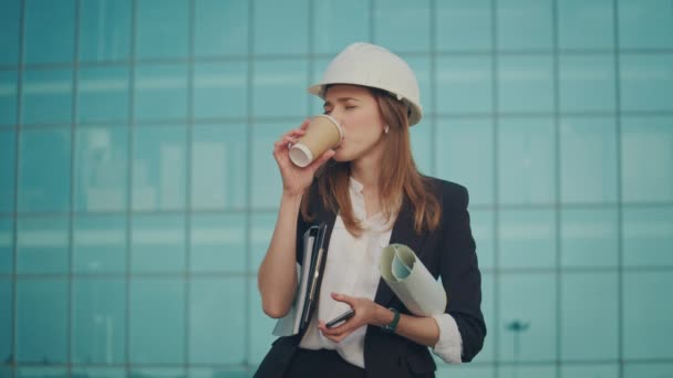一名工程师或建筑师 穿着正装 头戴耳机 一边站在现代玻璃商务区附近一边打电话一边拿着咖啡杯 咖啡休息时间室外 — 图库视频影像