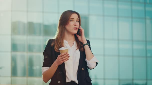 若い女性エンジニアまたはフォーマルスーツのアーキテクト コーヒーブレイクの間に立って電話で話す青いWindowsと建物の近く — ストック動画