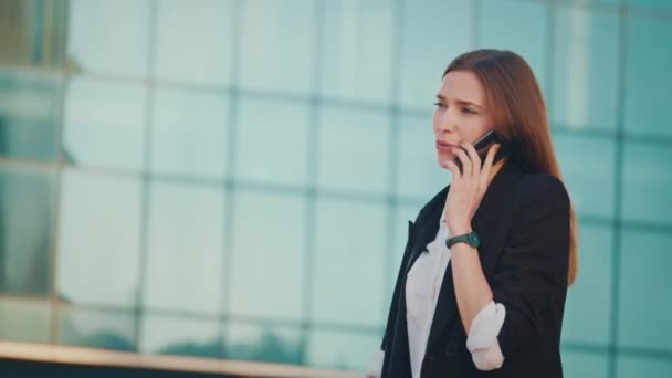 一个年轻成功的女商人穿着西装 在一个现代玻璃商务区边走边用智能手机交谈的画像 — 图库视频影像