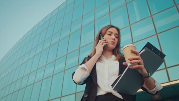 ハッピービジネスウーマンは 外のビジネスオフィスに立っている間 携帯電話のホールディングカップで話しています 人とアプリ テクノロジーとビジネス — ストック動画